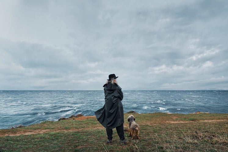 Person und Hund blicken über ein stürmisches Meer unter grauem Himmel. Person und Hund blicken über ein stürmisches Meer unter grauem Himmel.